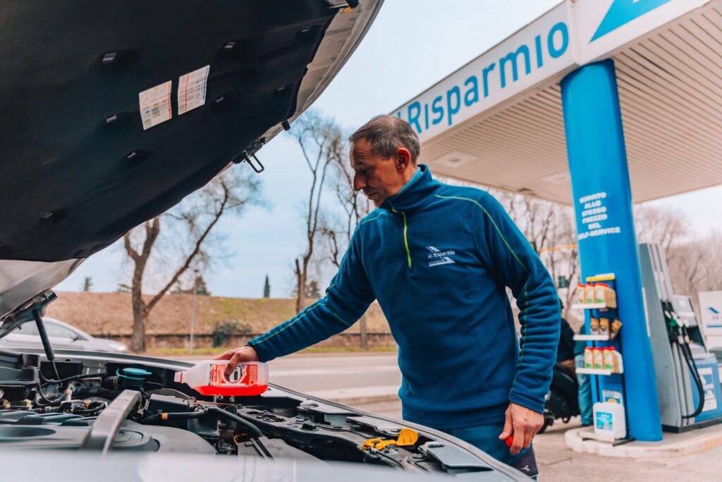 Addetto di una stazione di servizio utilizza un prodotto per il motore su un auto